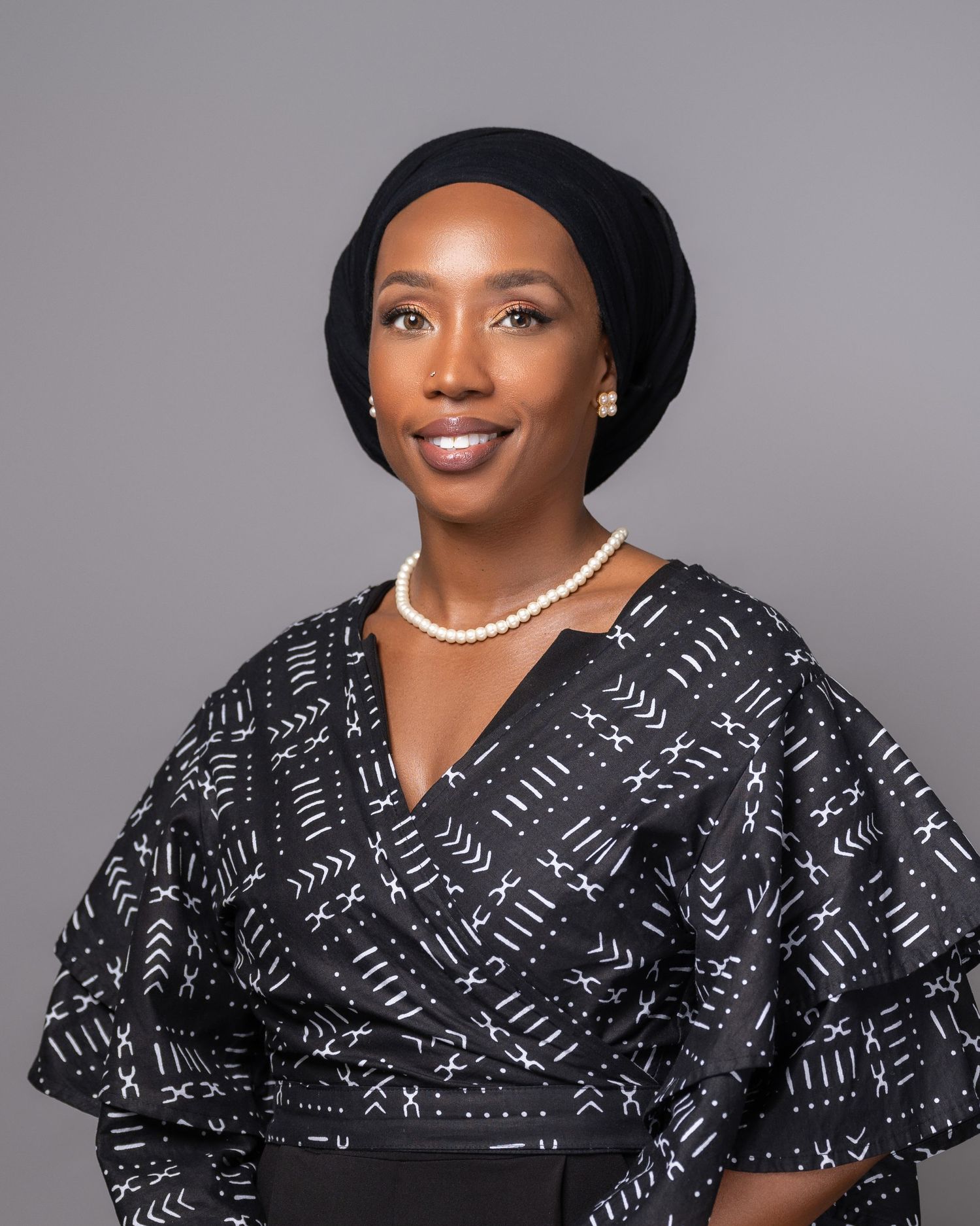 Professional portrait of person wearing black headwrap and pearl necklace with patterned black dress.