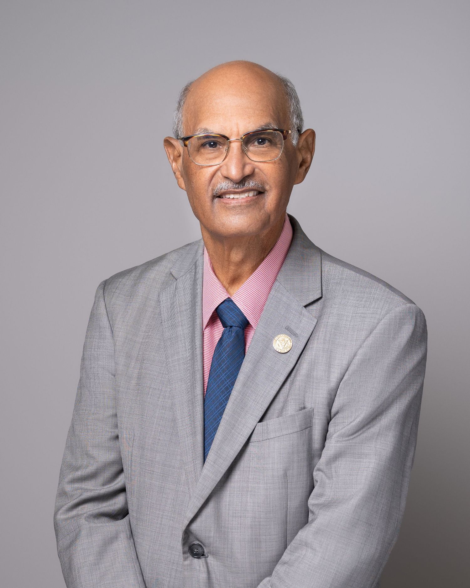 Professional headshot of person in gray suit with glasses against neutral background.