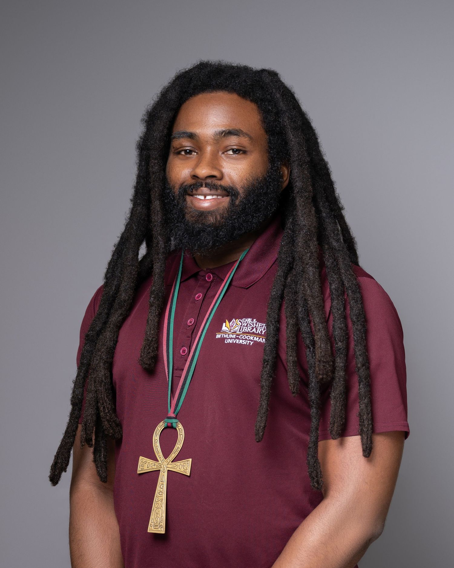 Portrait of person with dreadlocks wearing maroon shirt and ankh necklace.