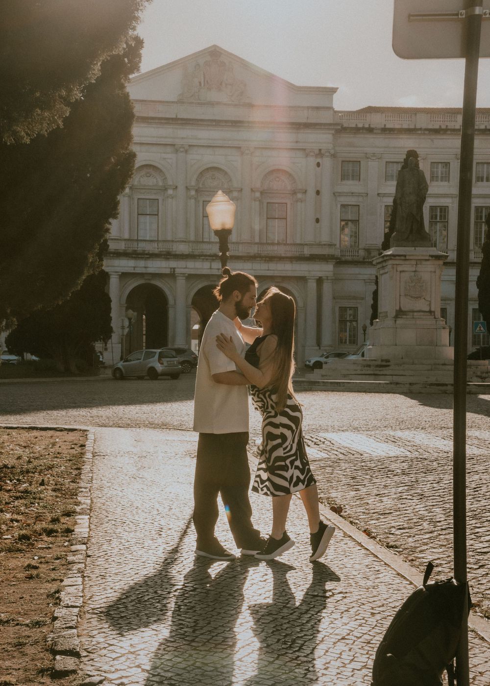 Couple dancing in front of classical building facade at sunset with lamp post glowing.