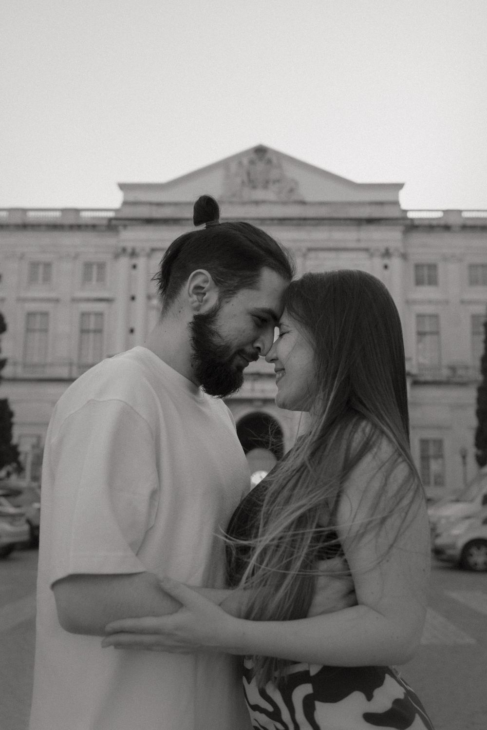 Romantic couple sharing an intimate moment in front of a historic building in black and white.