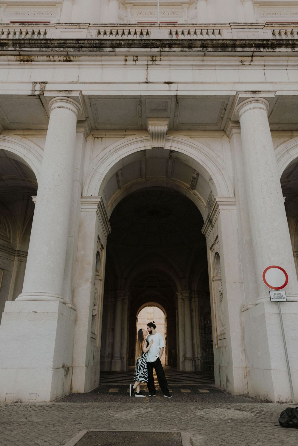 Silhouetted couple standing under grand white archway of classical architecture.