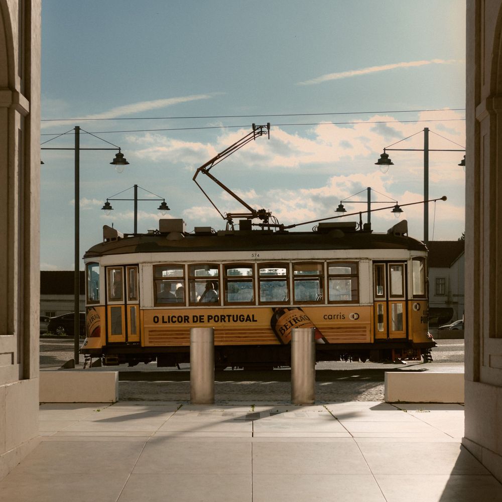 Vintage yellow tram car on tracks with overhead power lines against a blue sky with wispy clouds.