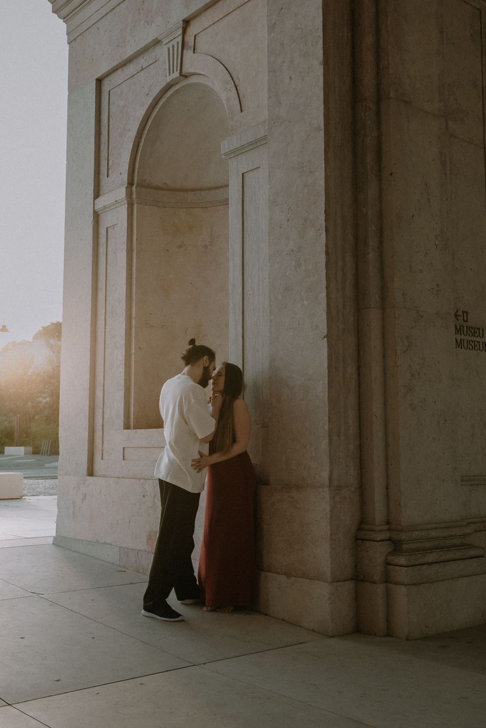 A couple sharing an intimate embrace against a classical stone building during golden hour.