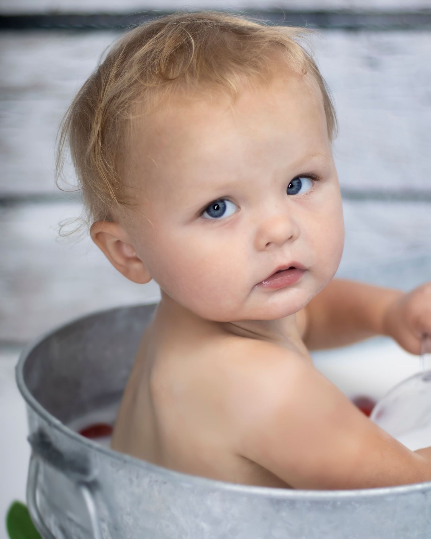 A baby girl looks over her shoulder from inside a milk bath