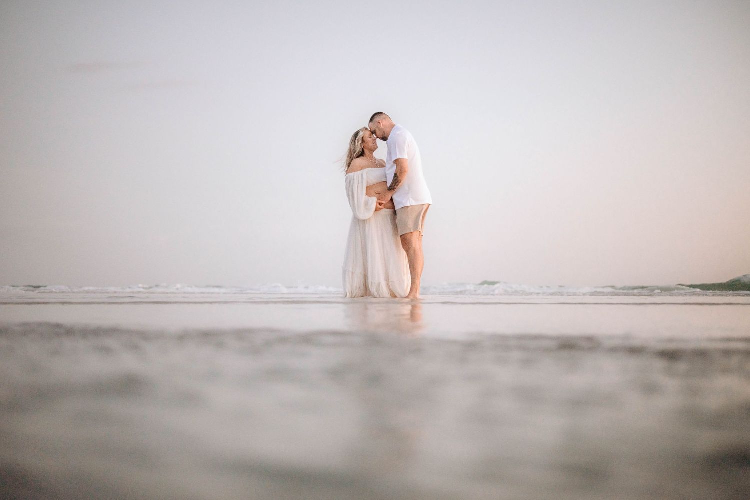 A romantic beach photoshoot during golden hour with soft waves in the background.