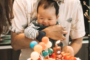 Baby smiling while reaching for colorful birthday cake decorations.