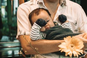 Sleeping baby held in arms with striped sleeves near orange flower.