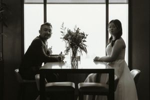 A black and white photo of a couple sitting at a table with a vase of flowers between them in a minimalist room.