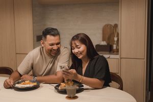 Couple sharing a casual dining moment while looking at a smartphone during mealtime at a table.