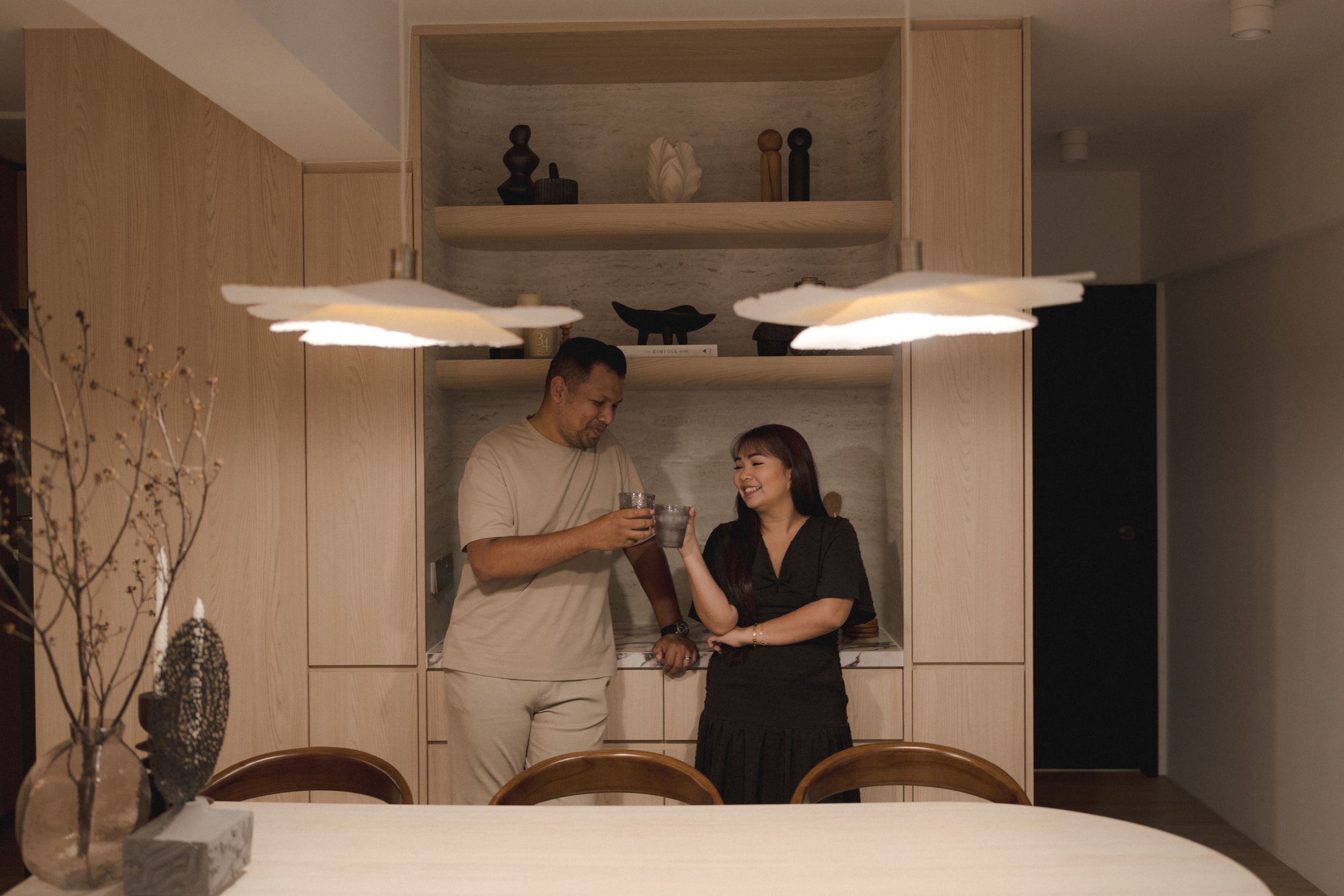 Two people standing at dining table under pendant lights in modern minimalist interior with built-in storage.