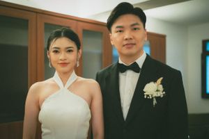 A formal couple in white gown and black tuxedo in an indoor setting.