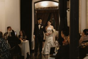 Elegant wedding reception entrance with guests seated at tables in a dimly lit venue.