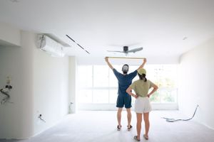 Two people celebrate in empty white room with raised arms looking at ceiling.