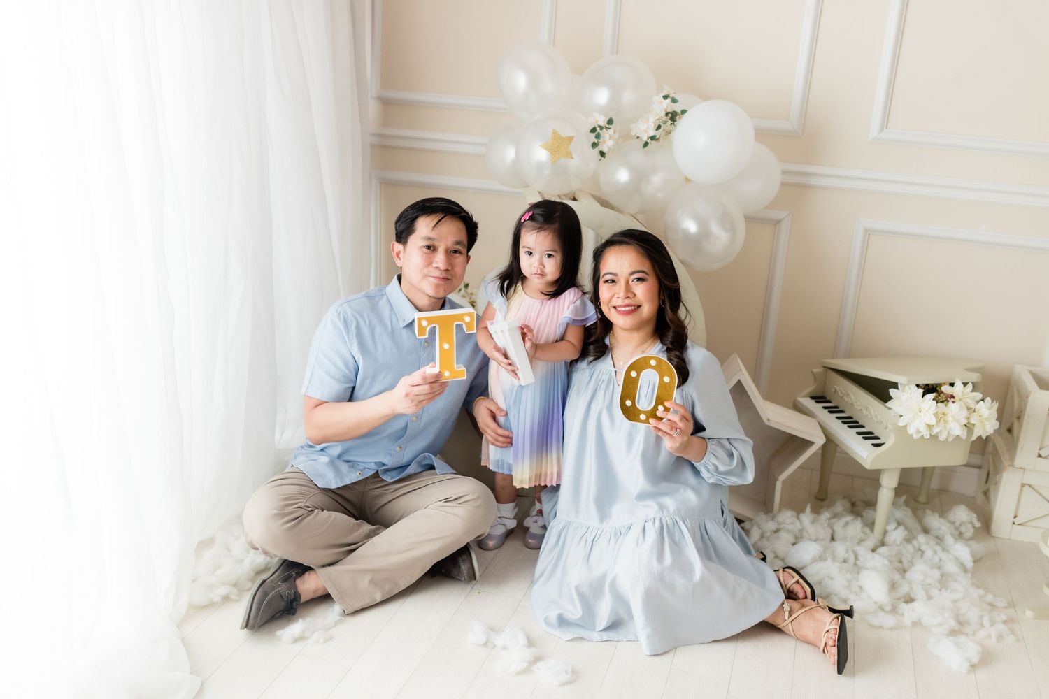 Family enjoying pizza together on floor with white balloons and elegant decor.