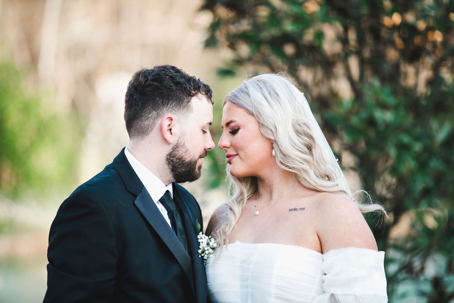 A tender moment between newlyweds outdoors with soft greenery in the background.