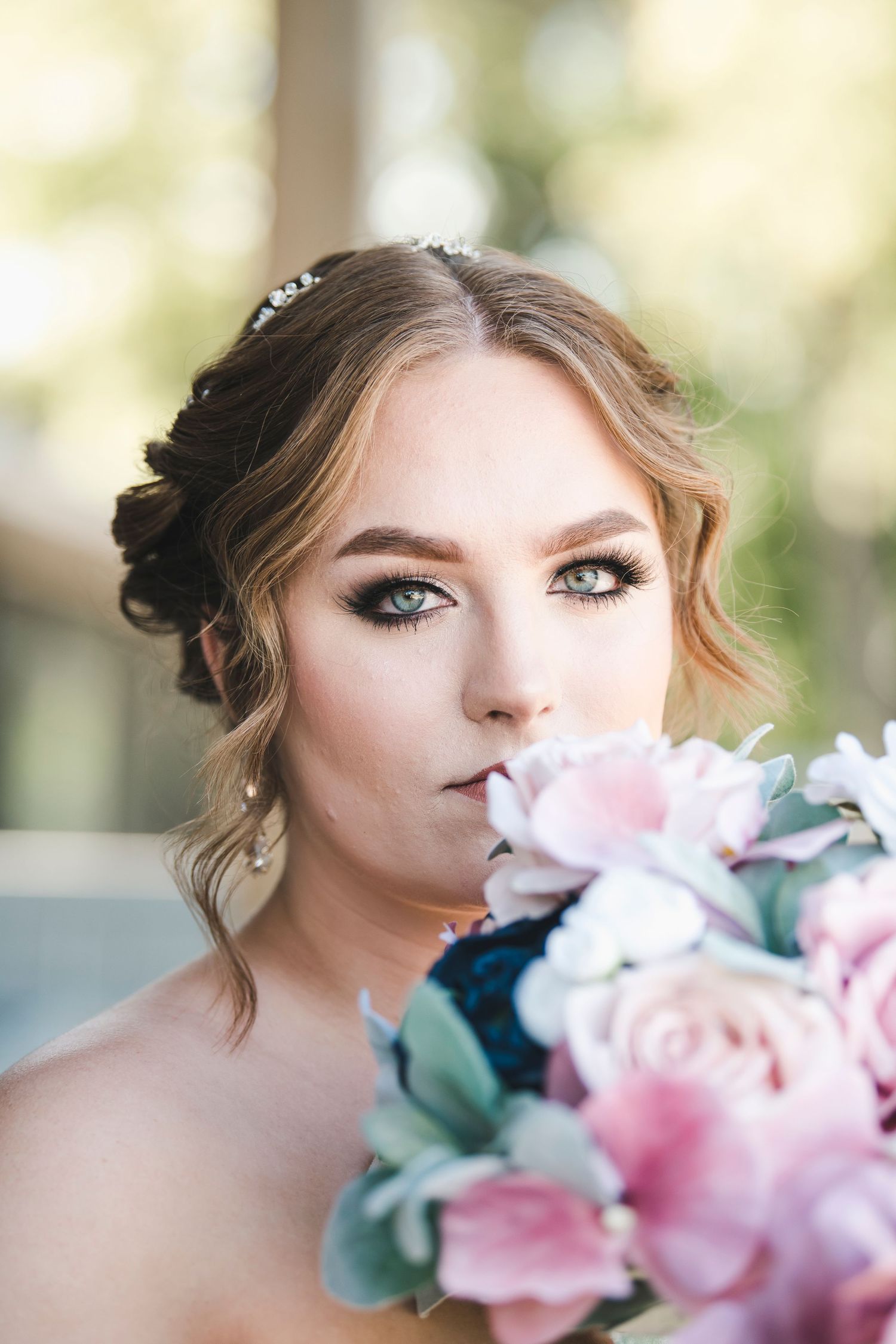 Closeup of bridal portrait with soft makeup and pink roses against blurred background.