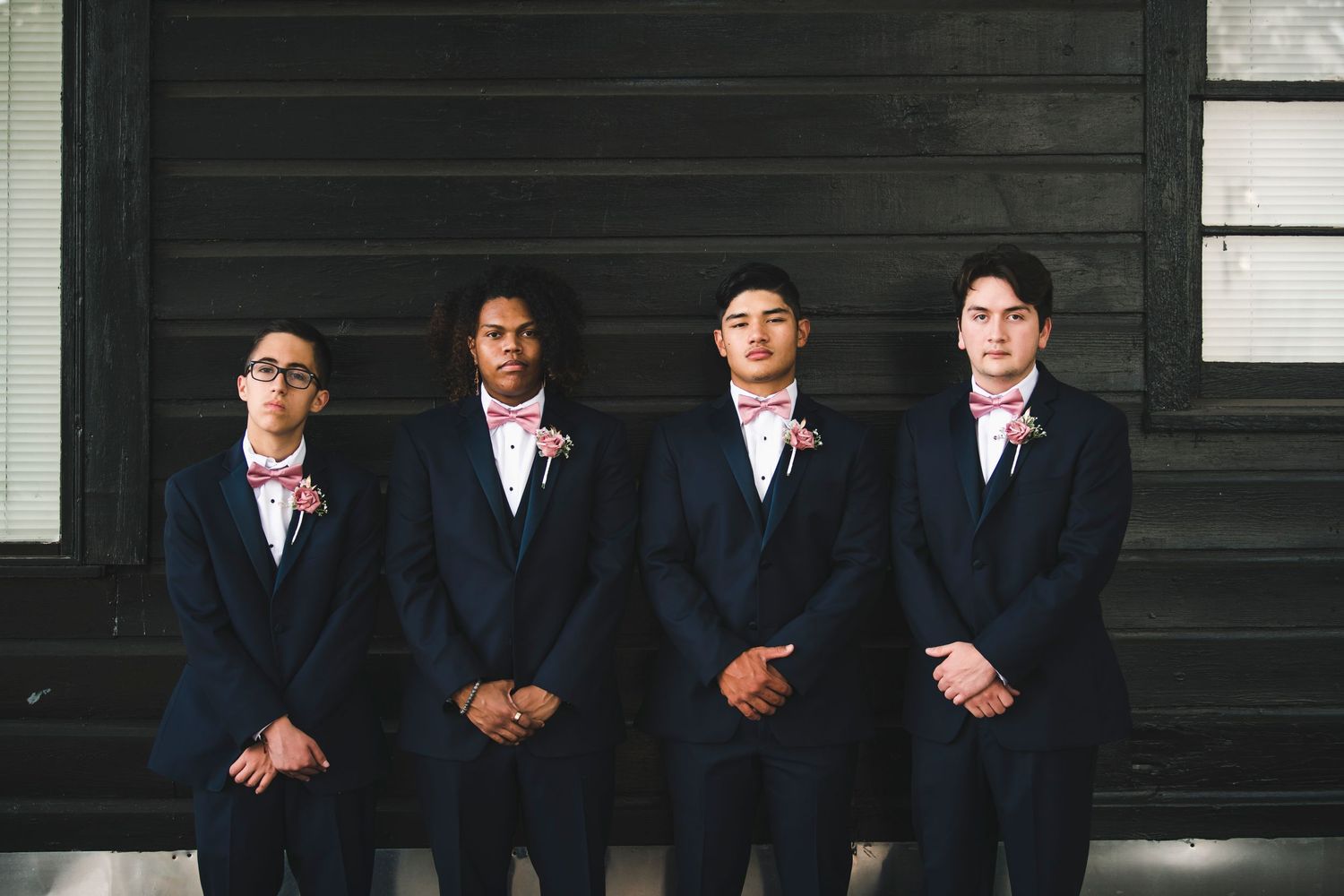 Groomsmen in navy suits pose against dark wooden wall for formal wedding portrait.