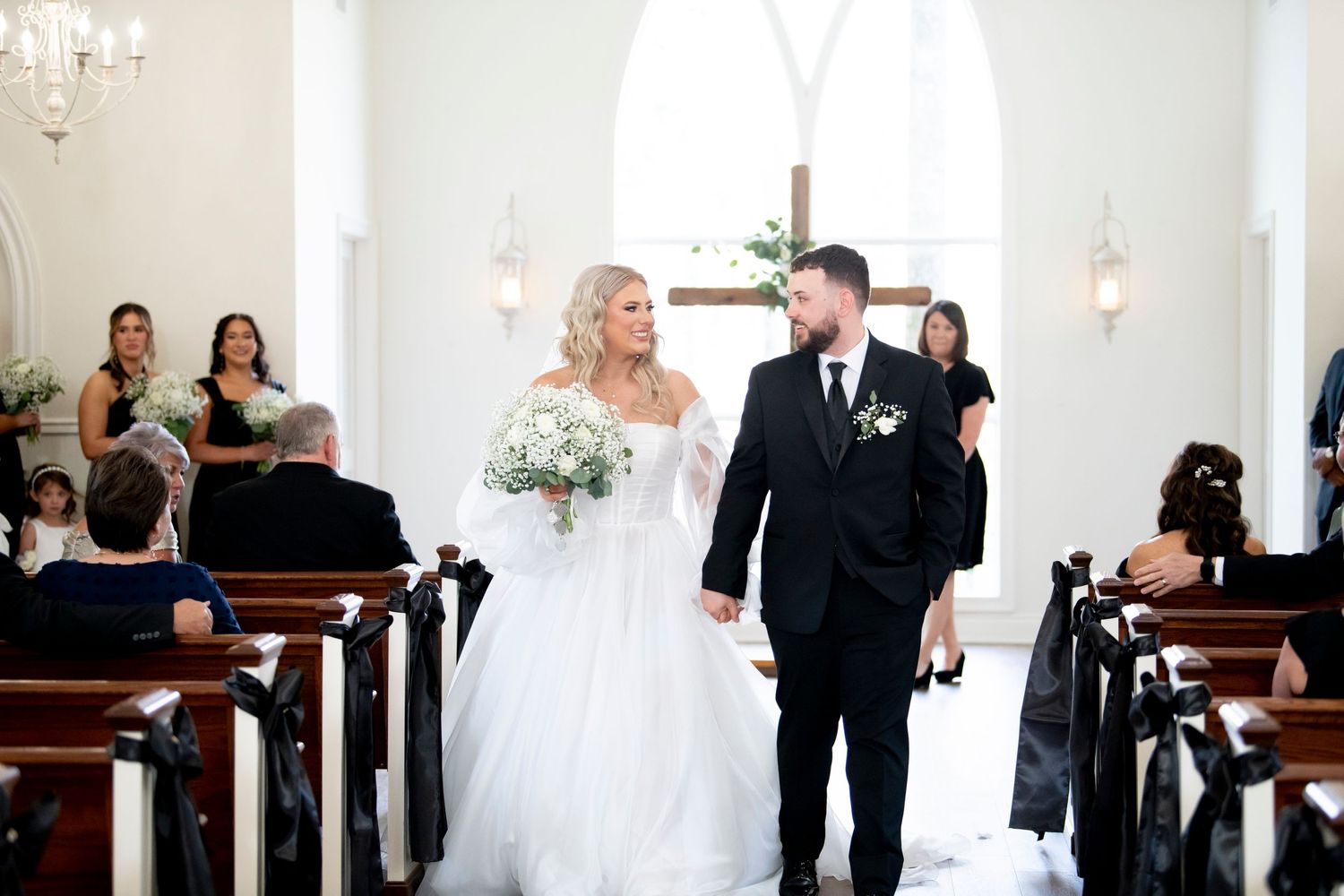 A newlywed couple walking down the aisle of a classic white chapel after their ceremony.