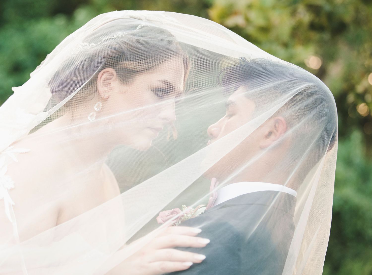 Romantic moment under wedding veil captured in soft, ethereal outdoor lighting.