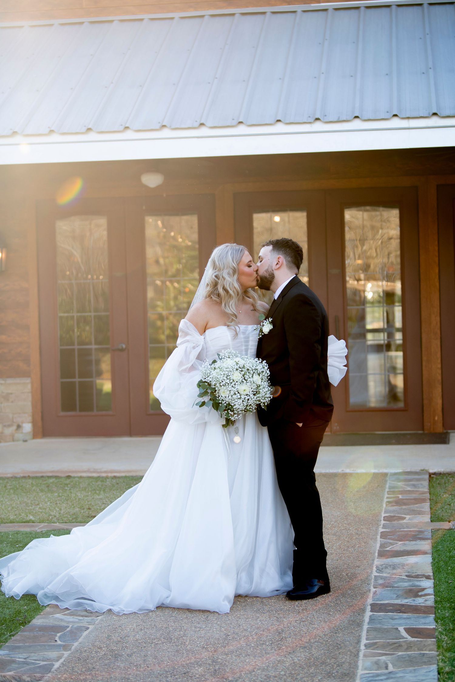 Romantic wedding portrait of newlyweds embracing outside a rustic venue at sunset.