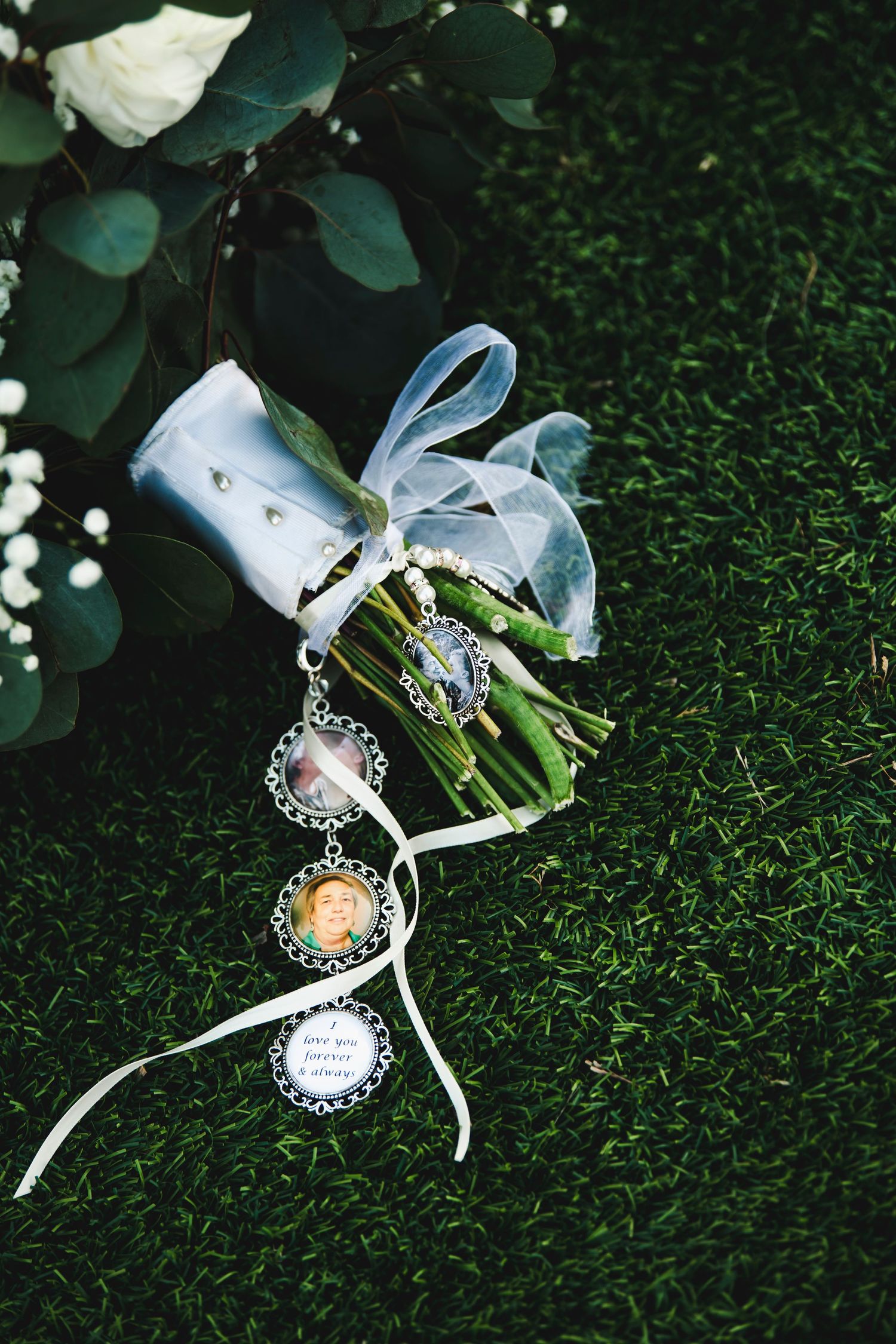 Wedding bouquet wrap decorated with vintage photo charms tied with blue ribbon on grass.