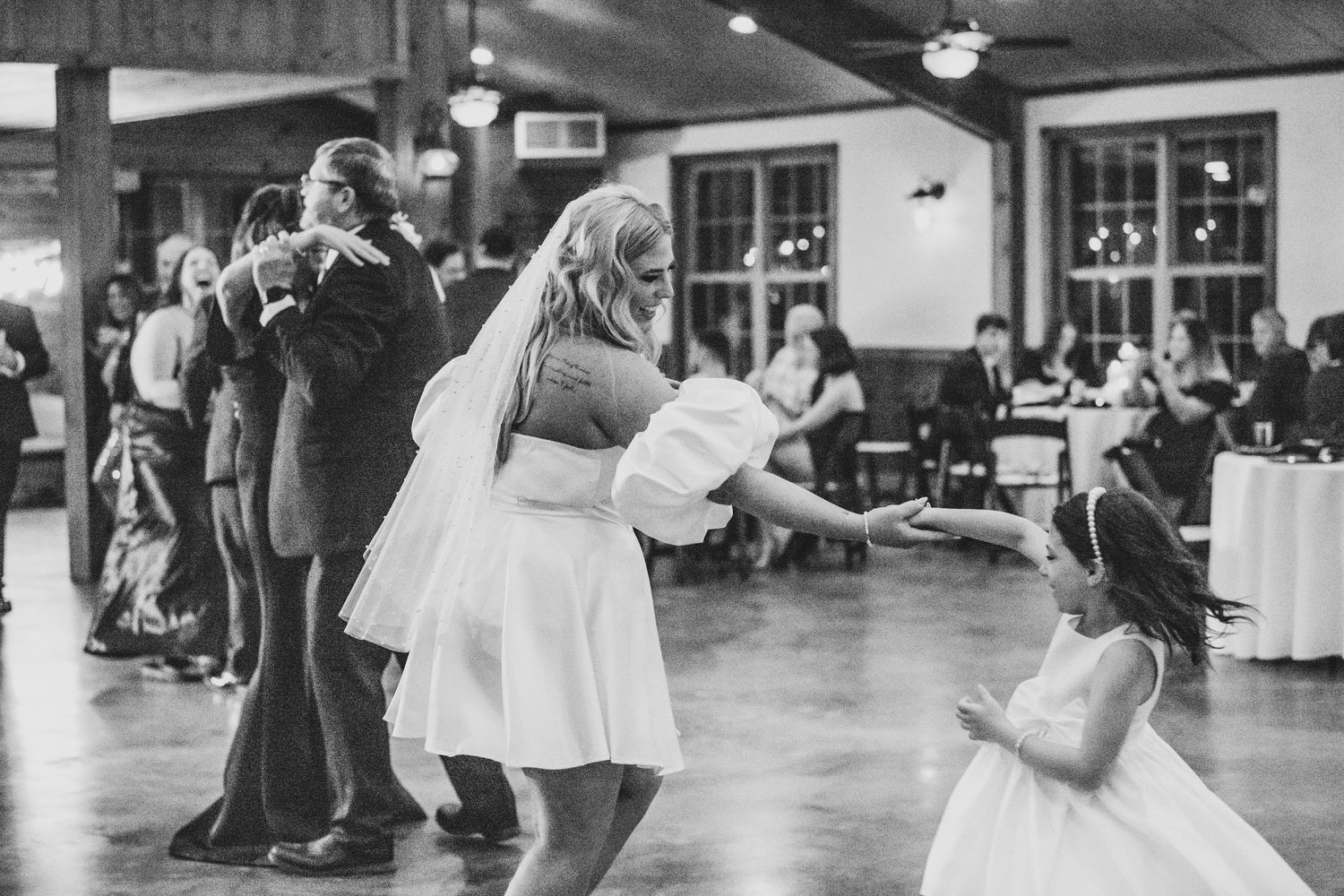 Black and white photo of wedding guests dancing at a reception with a young child in the foreground.