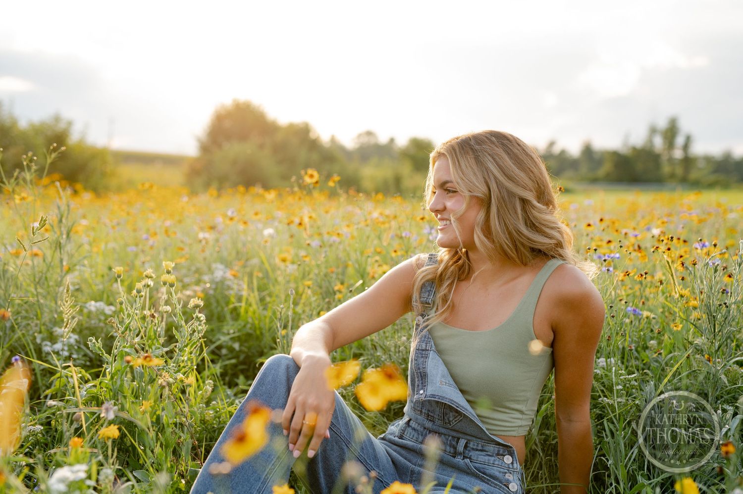 A candid portrait of someone sitting in a wildflower meadow wearing denim overalls at sunset.