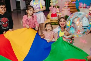 Children playing with a colorful parachute during an indoor celebration.