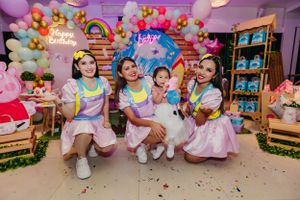 Group photo with matching pastel outfits against balloon arch and rainbow party decorations.