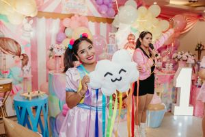 Party entertainer holding cloud-shaped prop against pink balloon backdrop.