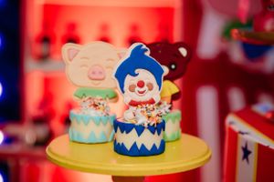 Decorative circus-themed cake toppers featuring clowns and animals on yellow stand.