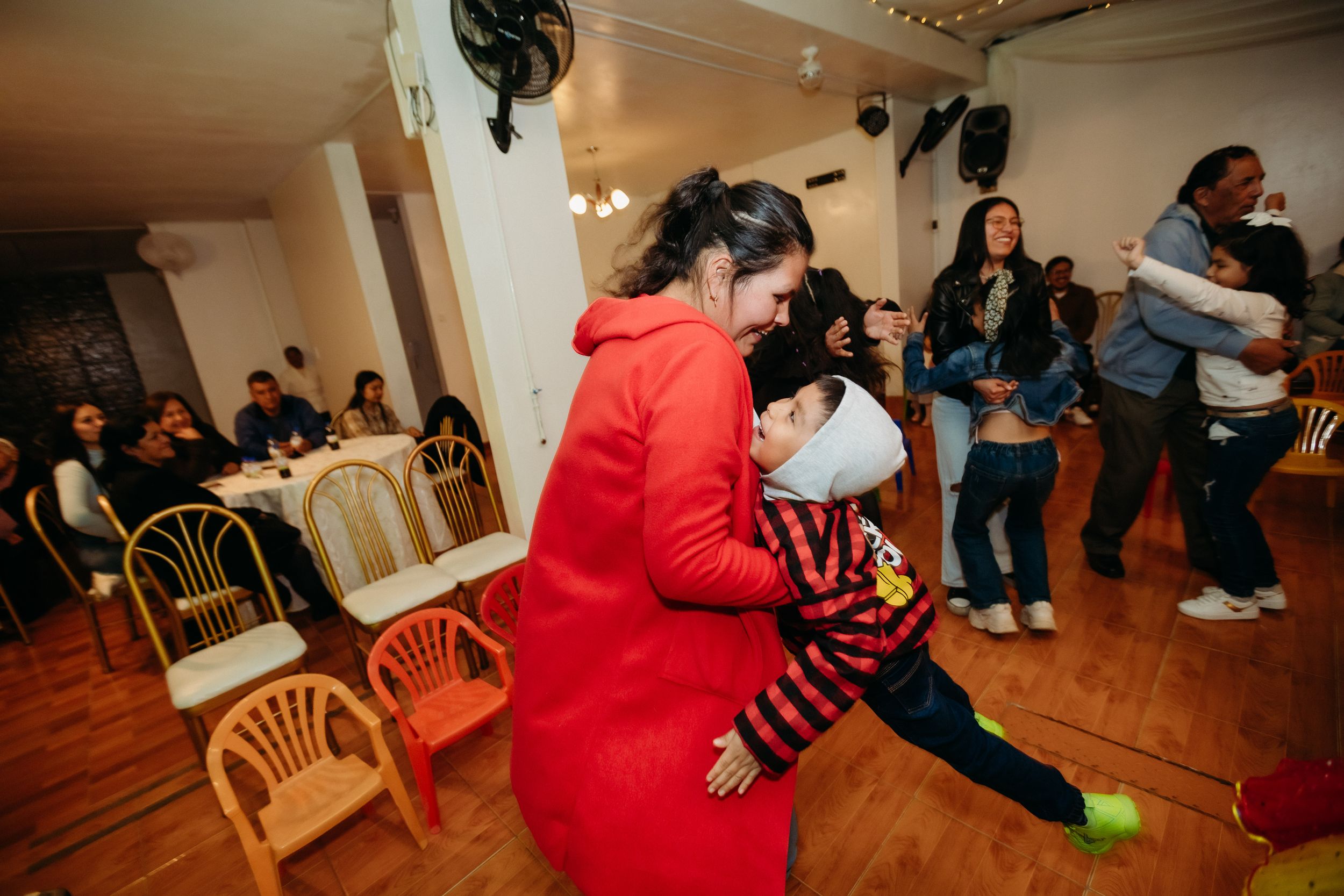 People enjoying a lively party in an indoor venue with wooden chairs and hardwood flooring.