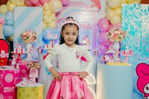 A young party celebrant in a pink and white dress posing in front of a colorful balloon display.