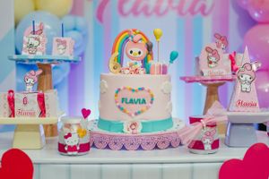 A pastel-colored birthday cake with rainbow decorations and the name Flavia displayed on the front.