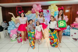 A group posing in colorful party outfits against a balloon-decorated background.