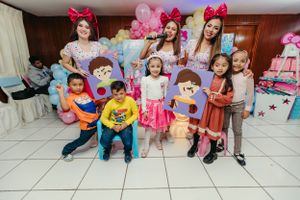 A celebration group photo with cartoon character cutouts and pink balloon decorations.