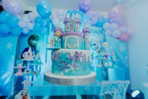 An elaborate blue and white tiered castle cake with winter decorations at a themed celebration.