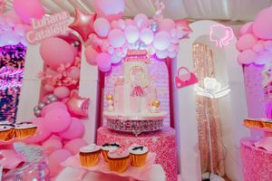Pink balloon arch and party decorations with cupcakes at a Barbie-themed celebration.