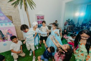 Children playing and celebrating at a party with indoor grass flooring and festive decorations.