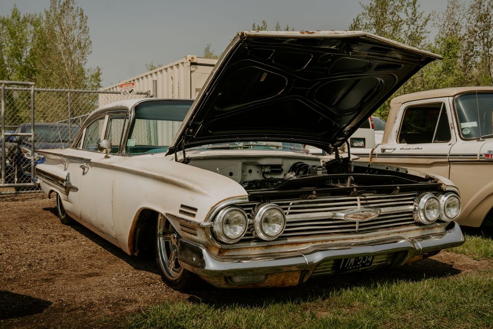 Classic white 1950s Chevrolet with hood up displaying engine bay in outdoor setting.
