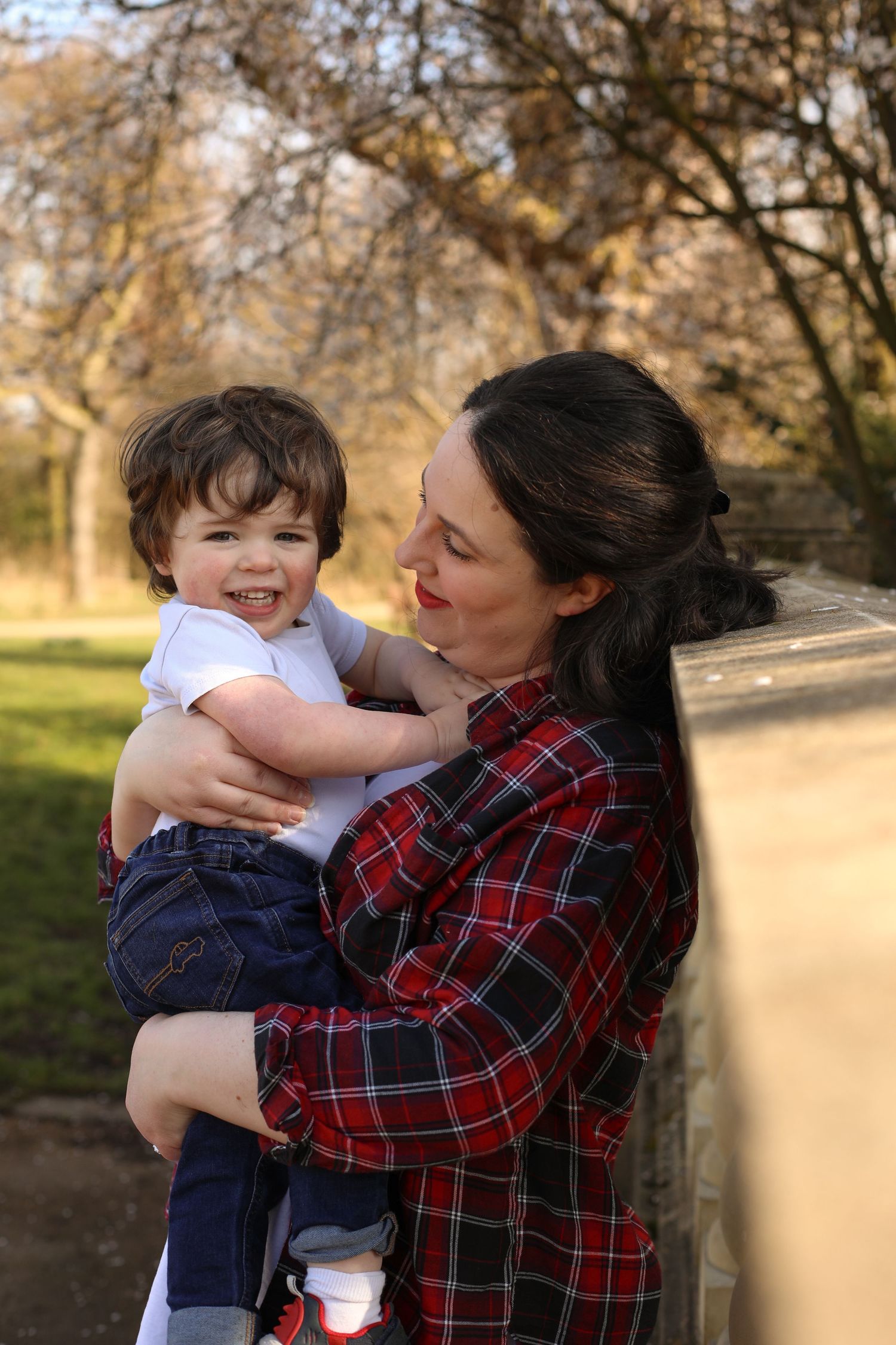 A child laughs joyfully while being held outdoors by someone wearing a red plaid shirt on an autumn day.