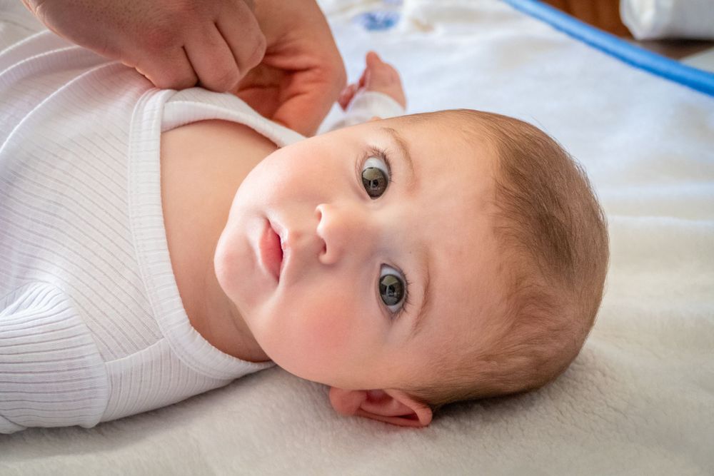 Close-up of a newborn baby with blue eyes lying on white blanket during early checkup.