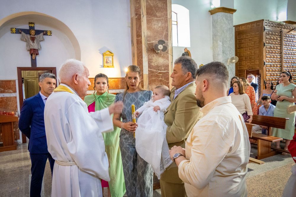 Catholic baptism ceremony with priest, parents, and guests gathered around baby in church.