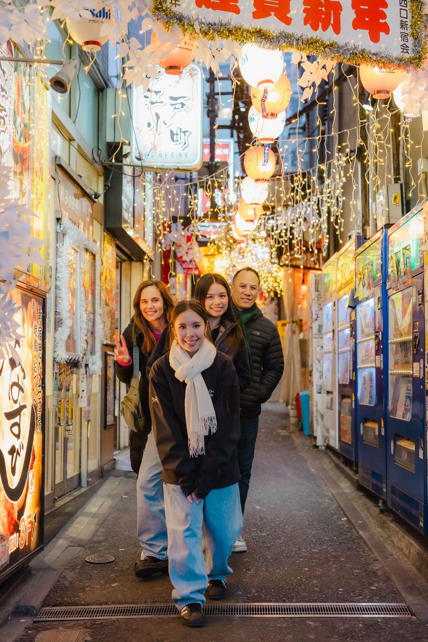 A group poses in a narrow alley decorated with festive lights and Chinese New Year decorations.