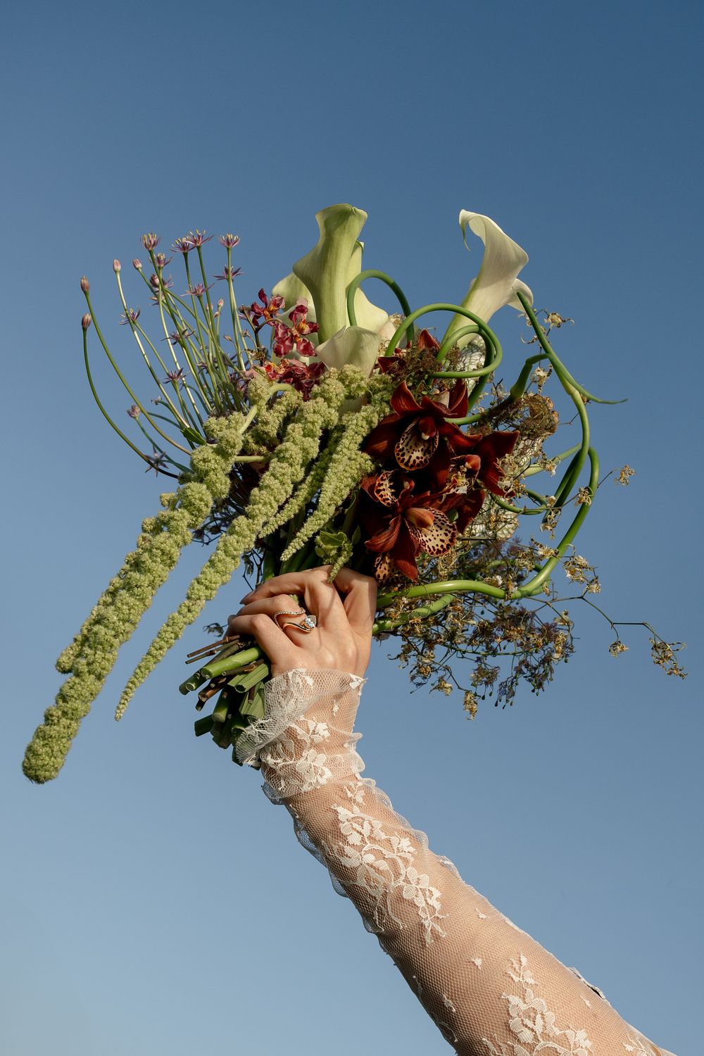 A unique wedding bouquet with calla lilies and wild flowers held against a blue sky.