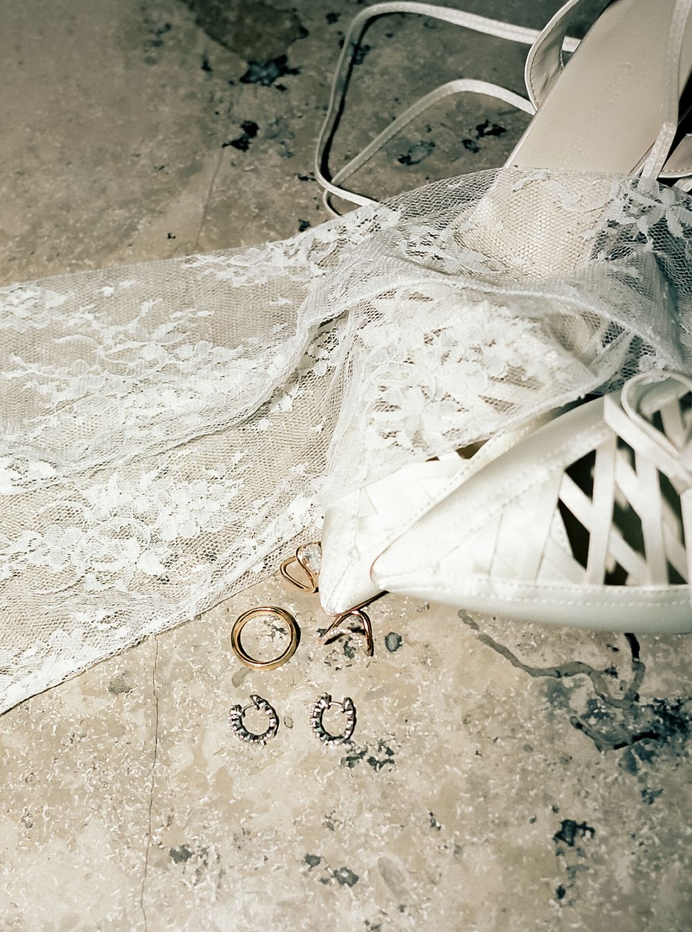 Wedding rings and bridal shoes photographed on textured concrete surface.