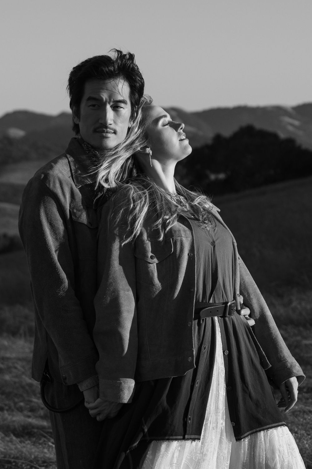 Artistic black and white portrait of a couple in romantic poses against a scenic backdrop.
