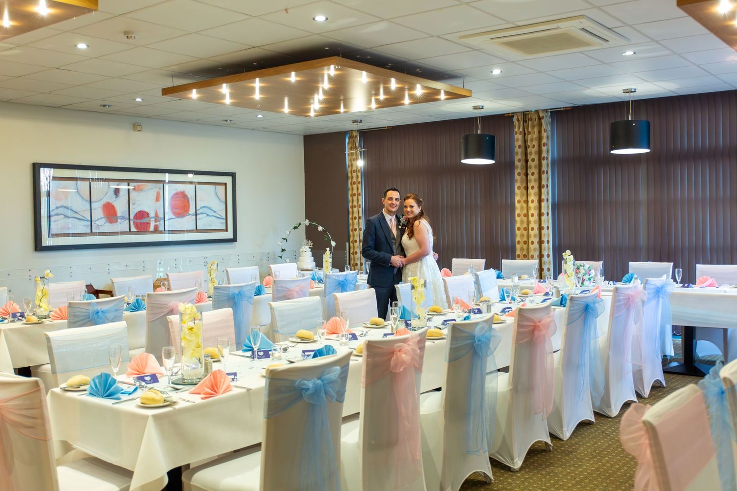 An elegantly decorated wedding reception room with white chair covers and blue table settings.