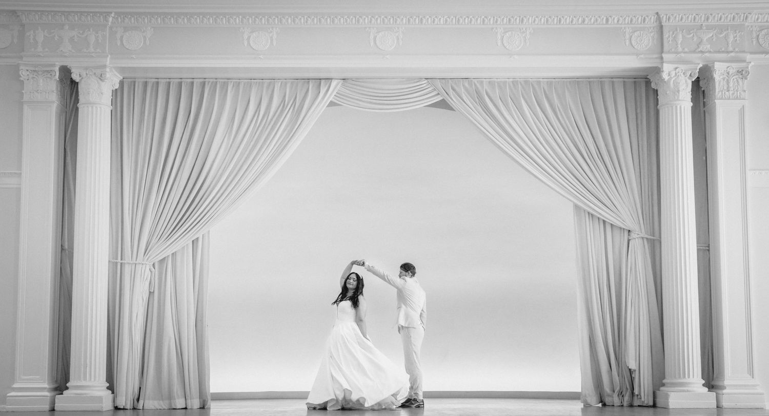 Elegant couple dances behind sheer white curtains in a classic ballroom setting.